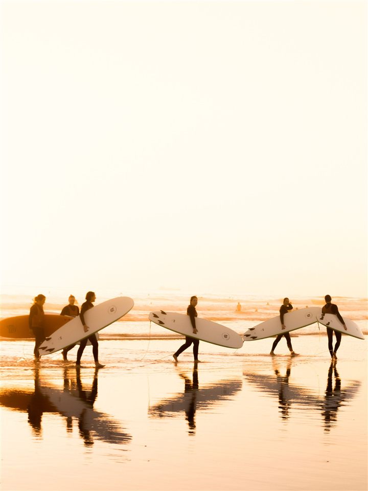 Two surfers walking along the shoreline at sunset, boards under their arms