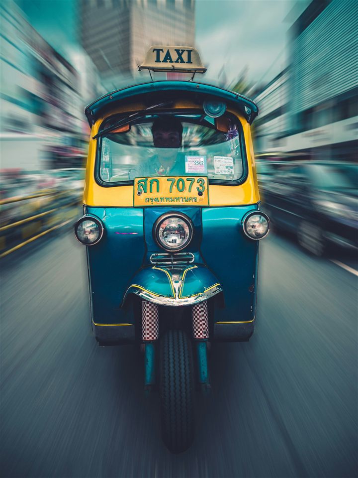 A three-wheeled tuk-tuk taxi in motion on a city street