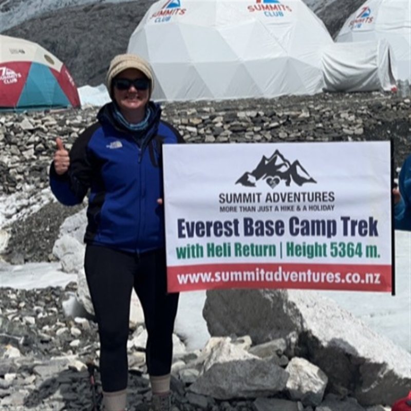 Olivia, founder of Summit Adventures, giving a thumbs up at Everest Base Camp next to a Summit Adventures trek sign